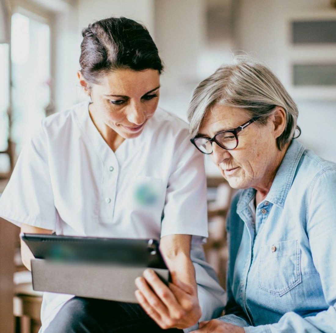 A nurse visiting an older woman at home and helping her with the tablet